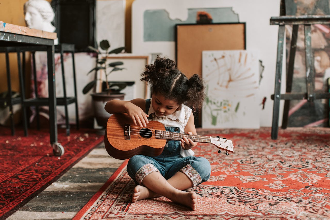 Mastering the First Impression: Your intriguing post title goes here Adorable young girl sitting on the floor playing a ukulele in a vibrant art studio.